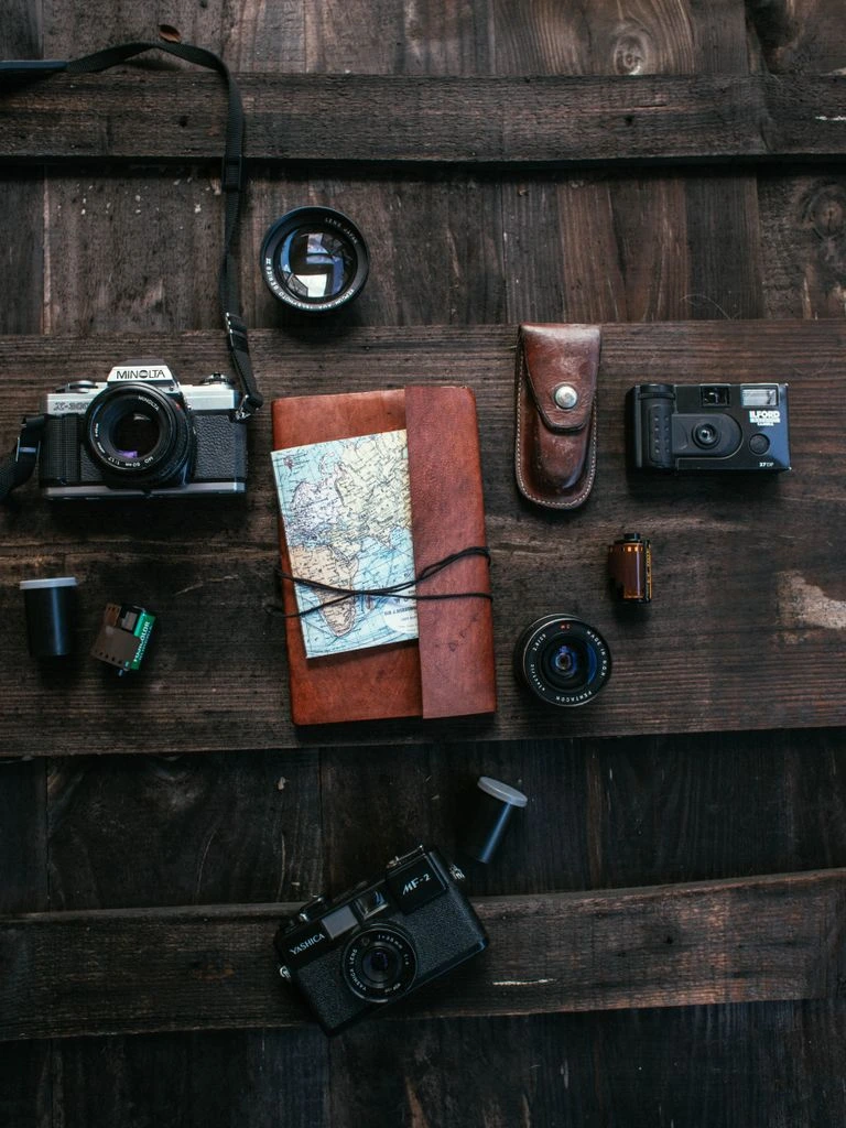 A flat-lay of three notebooks, a camera and a glass of water.